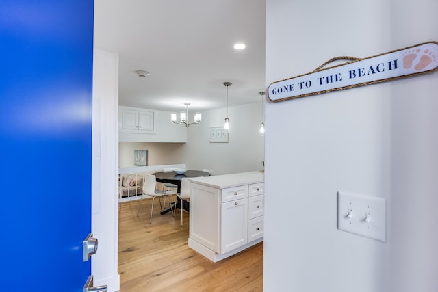 kitchen featuring light wood-style floors, light countertops, white cabinetry, a chandelier, and decorative light fixtures