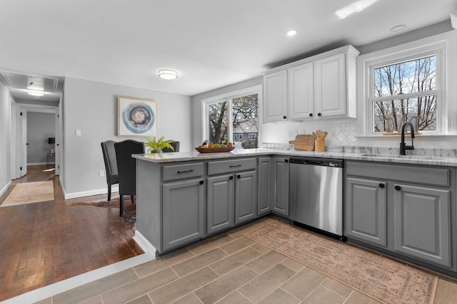 kitchen with dishwasher, light stone counters, a peninsula, gray cabinets, and a sink