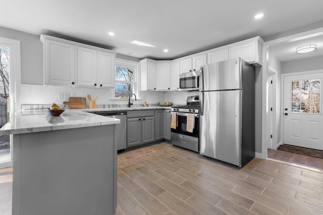 kitchen featuring light stone counters, gray cabinets, appliances with stainless steel finishes, white cabinetry, and a peninsula