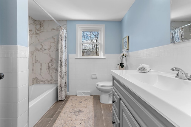 bathroom featuring tile walls, visible vents, toilet, wainscoting, and vanity