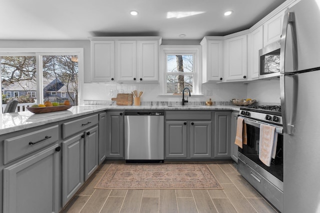 kitchen with appliances with stainless steel finishes, wood finish floors, gray cabinets, and a sink