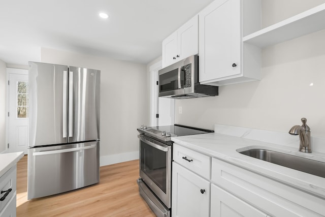 kitchen with white cabinetry, stainless steel appliances, light hardwood / wood-style floors, sink, and light stone counters