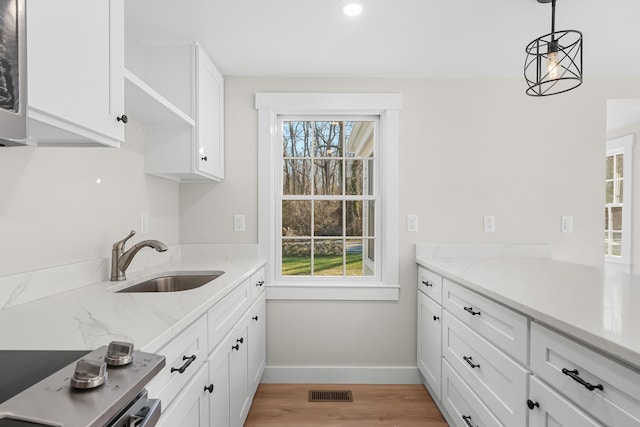 kitchen with light stone countertops, white cabinets, sink, hanging light fixtures, and light hardwood / wood-style flooring