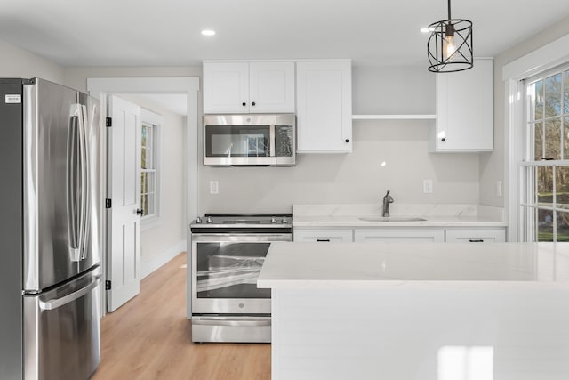 kitchen featuring white cabinets, stainless steel appliances, sink, hanging light fixtures, and light wood-type flooring