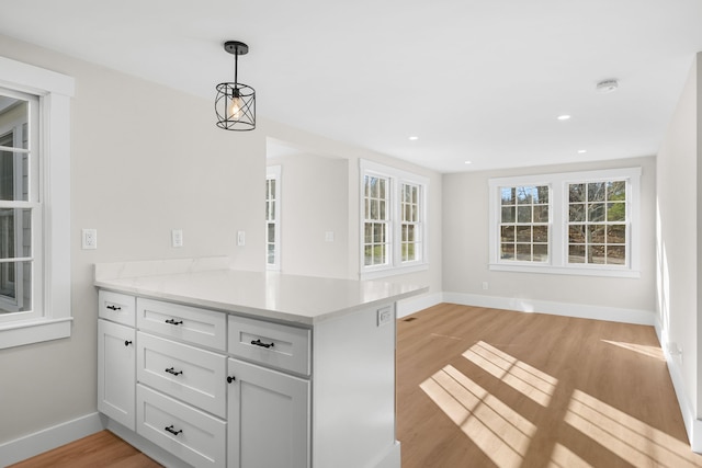 kitchen with light stone countertops, white cabinets, decorative light fixtures, kitchen peninsula, and light hardwood / wood-style flooring