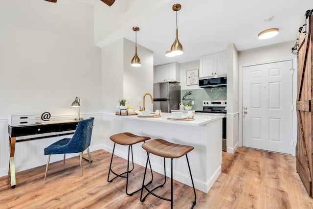 kitchen with appliances with stainless steel finishes, a barn door, a peninsula, white cabinets, and a breakfast bar area