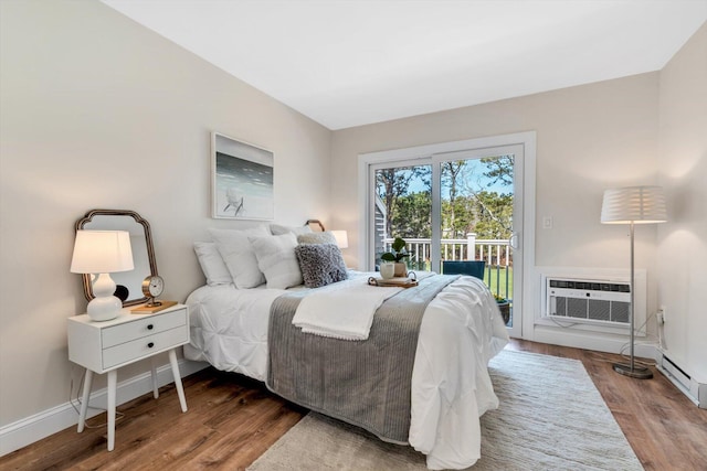 bedroom with access to outside, wood finished floors, a wall mounted air conditioner, baseboards, and a baseboard heating unit