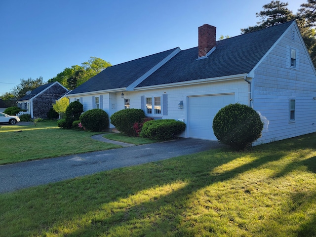 view of front facade featuring aphalt driveway, a shingled roof, a front yard, an attached garage, and a chimney