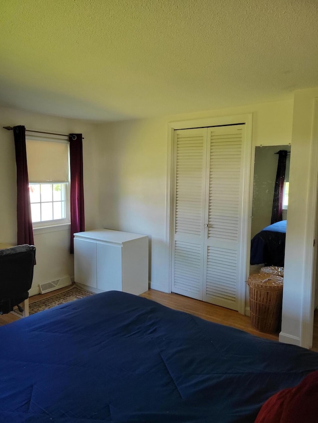 bedroom featuring visible vents, a textured ceiling, a closet, and wood finished floors