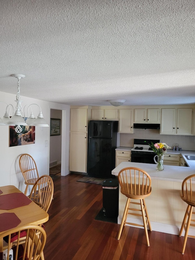 kitchen with black appliances, under cabinet range hood, a peninsula, light countertops, and dark wood-style flooring