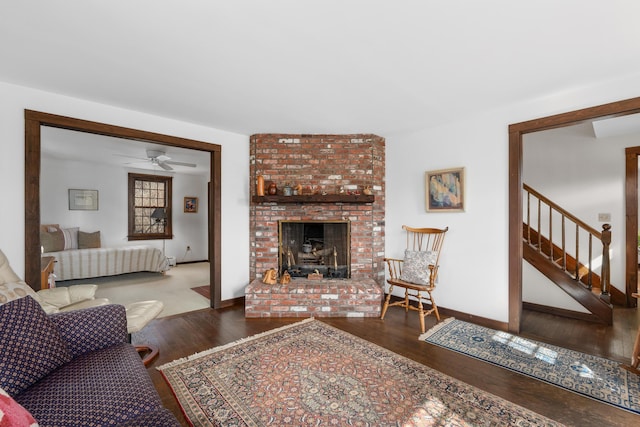 living area featuring baseboards, stairs, a fireplace, wood finished floors, and a ceiling fan