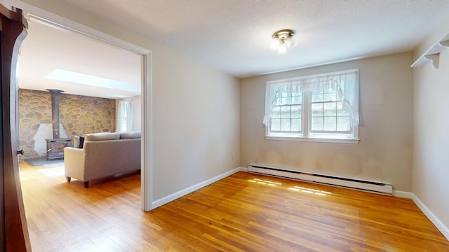 10 Freeman Rd, Yarmouth Port, MA 02675 - empty room with a baseboard radiator, a wood stove, wood finished floors, and a textured ceiling