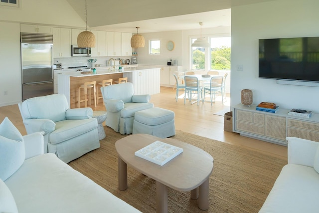 living room featuring sink, light hardwood / wood-style flooring, and lofted ceiling