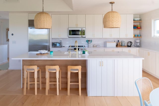 kitchen with decorative light fixtures, decorative backsplash, high end fridge, and an island with sink