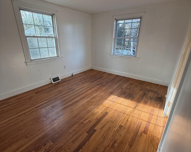 empty room with visible vents, baseboards, and dark wood finished floors