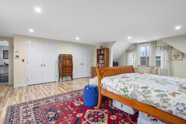 bedroom featuring multiple closets, lofted ceiling, and light hardwood / wood-style floors