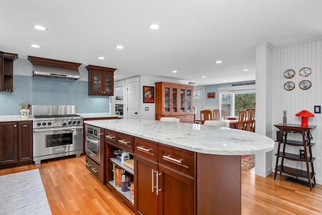 kitchen featuring a kitchen bar, light wood-type flooring, a kitchen island, stainless steel appliances, and wall chimney range hood