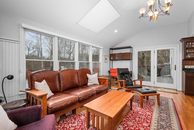 living room featuring a healthy amount of sunlight, vaulted ceiling with skylight, light hardwood / wood-style floors, and a notable chandelier