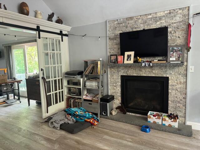 155 Mitchells Way, Barnstable, MA 02601 - living area featuring wood finished floors, vaulted ceiling, a stone fireplace, and a barn door