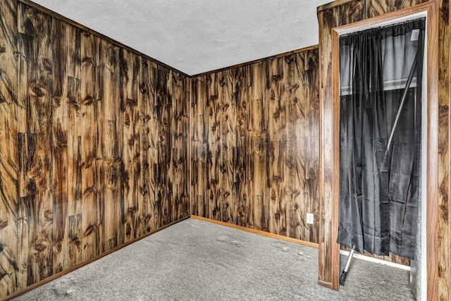 carpeted empty room with wooden walls and a textured ceiling