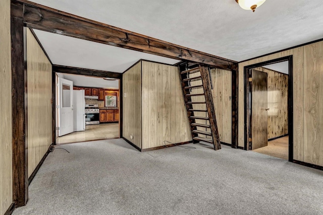 interior space featuring wooden walls, light carpet, a textured ceiling, and beam ceiling