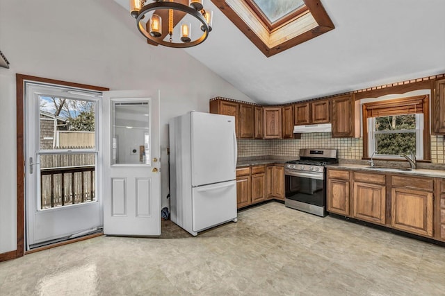 kitchen with stainless steel gas stove, sink, backsplash, white refrigerator, and hanging light fixtures