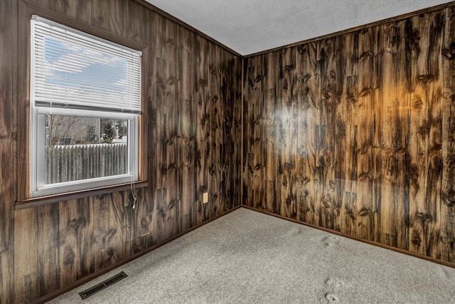 carpeted empty room featuring ornamental molding, a textured ceiling, and wood walls