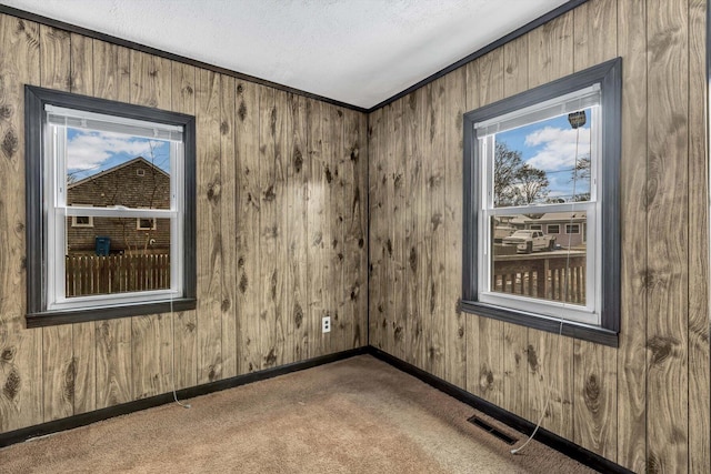 unfurnished room with wooden walls, ornamental molding, carpet flooring, and a textured ceiling