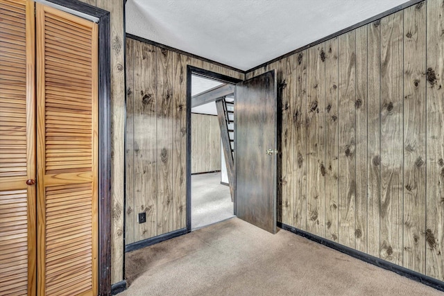 carpeted spare room with ornamental molding, a textured ceiling, and wood walls