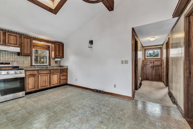 kitchen with vaulted ceiling with skylight, sink, decorative backsplash, and stainless steel gas stove