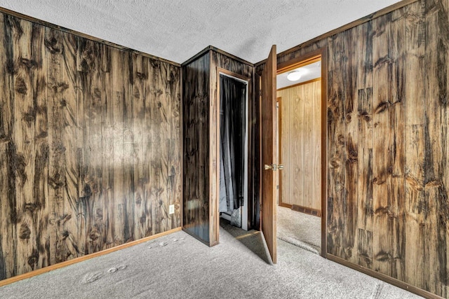 unfurnished room featuring wooden walls, a textured ceiling, and carpet flooring