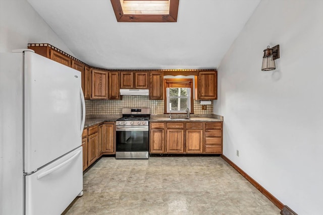 kitchen with sink, a skylight, stainless steel range with gas stovetop, white refrigerator, and tasteful backsplash