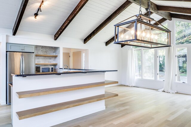 kitchen featuring appliances with stainless steel finishes, rail lighting, dark stone countertops, light hardwood / wood-style flooring, and vaulted ceiling with beams