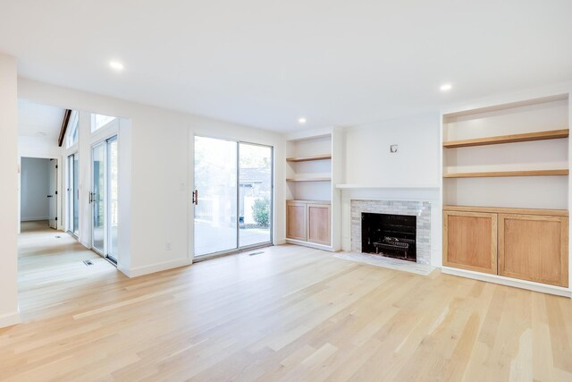 unfurnished living room with built in shelves, light hardwood / wood-style flooring, and plenty of natural light