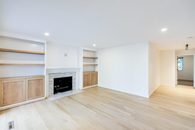 unfurnished living room featuring built in shelves and light hardwood / wood-style floors