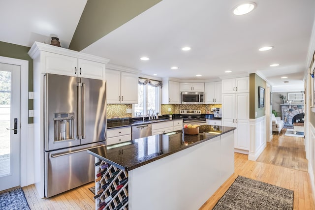 kitchen featuring light wood-style flooring, a sink, decorative backsplash, stainless steel appliances, and white cabinetry