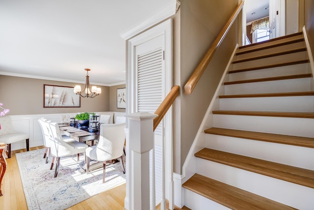 staircase featuring a decorative wall, crown molding, a wainscoted wall, wood finished floors, and a notable chandelier