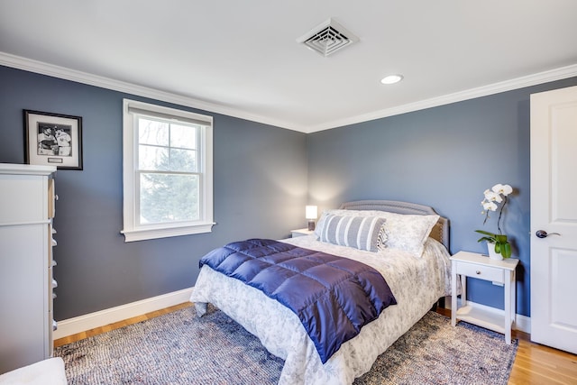 bedroom with crown molding, wood finished floors, visible vents, and baseboards