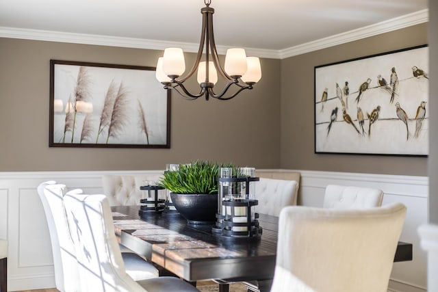 dining area featuring crown molding, a decorative wall, a notable chandelier, and a wainscoted wall