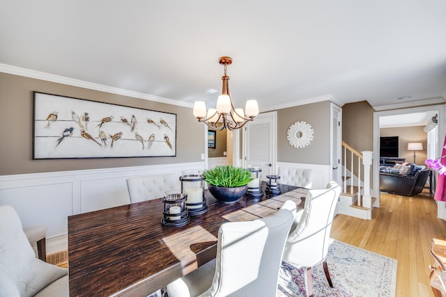 dining room with a notable chandelier, crown molding, light wood-type flooring, and stairs