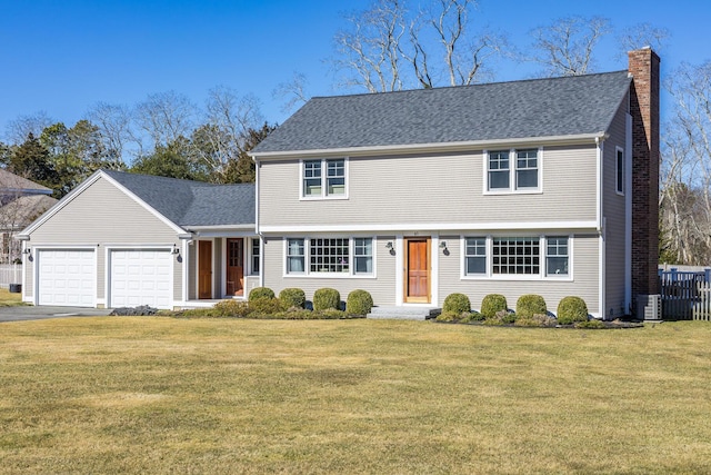 colonial home with an attached garage, a chimney, and a front yard