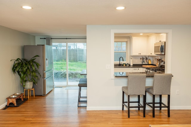 kitchen with a breakfast bar area, white cabinetry, a sink, dark countertops, and stainless steel appliances