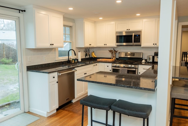 kitchen with a sink, decorative backsplash, stainless steel appliances, light wood-style floors, and white cabinets