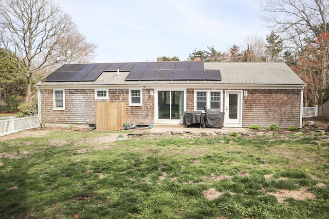 back of house with roof mounted solar panels, a chimney, a yard, and a fenced backyard