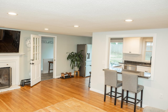 kitchen featuring light wood-style floors, a fireplace with raised hearth, a kitchen breakfast bar, dark countertops, and appliances with stainless steel finishes