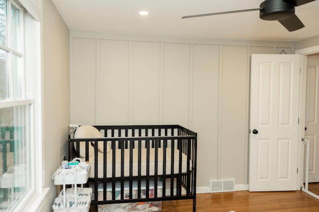 bedroom featuring wood finished floors, visible vents, a decorative wall, and a crib