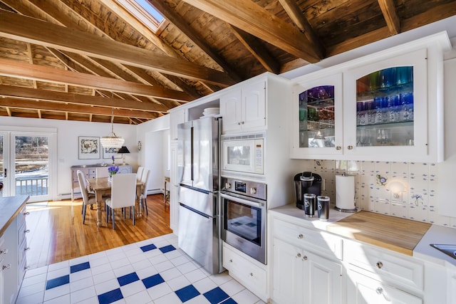 kitchen featuring white cabinets, lofted ceiling with beams, glass insert cabinets, appliances with stainless steel finishes, and light countertops