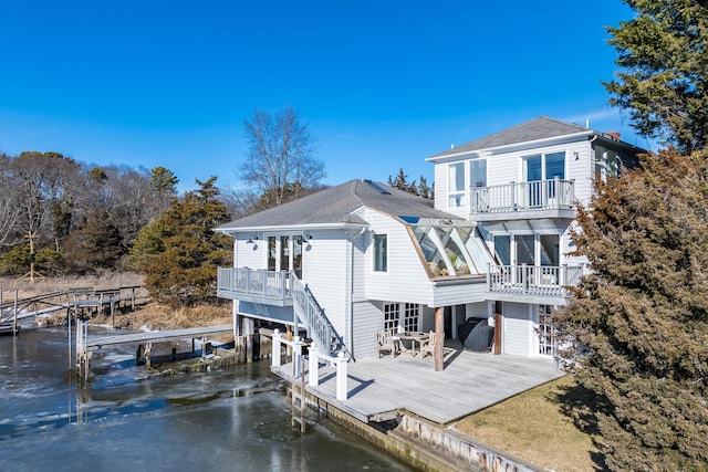 rear view of house featuring a balcony, boat lift, a shingled roof, and a deck with water view