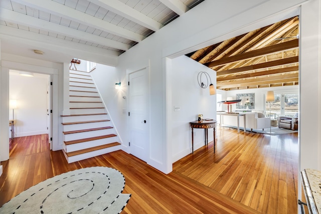 corridor with stairs, lofted ceiling with beams, wood-type flooring, and baseboards