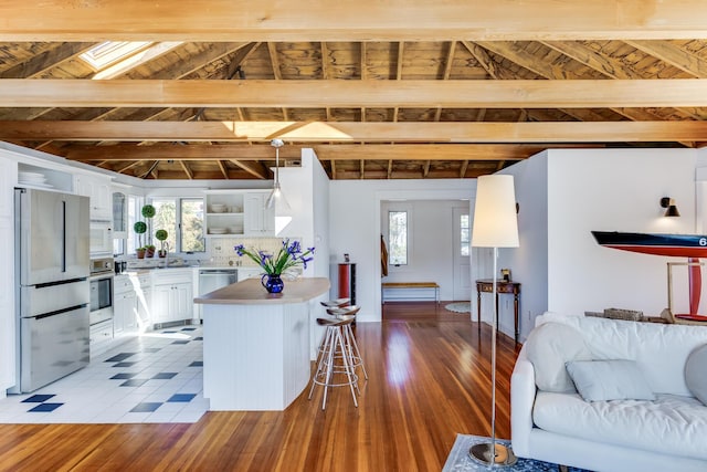 kitchen featuring stainless steel appliances, a kitchen island, white cabinetry, open shelves, and a kitchen bar